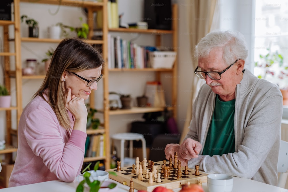 An adult daughter visiting her senior father at home and playing chess together.