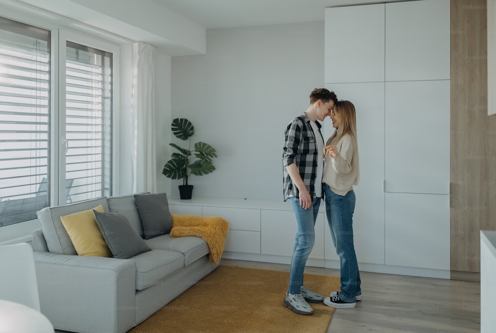 A cheerful young couple in their new apartment, standing and holding keys. Conception of moving.