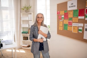 A job center employee with file form standing in front of employment noticeboard.