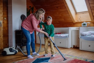 Un niño con síndrome de Down con su madre limpiando la aspiradora en casa
