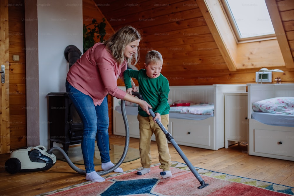 A boy with Down syndrome with his mother vacuum cleaning at home