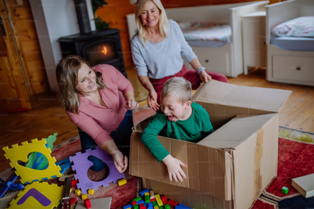 Un niño con síndrome de Down con su madre y su abuela jugando juntos a la caja en casa.