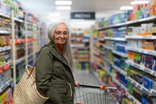 Una mujer mayor de pie y comprando en el supermercado.