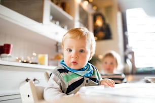 Cute baby boy sitting in highchair at Christmas time. Two small children in a kitchen.