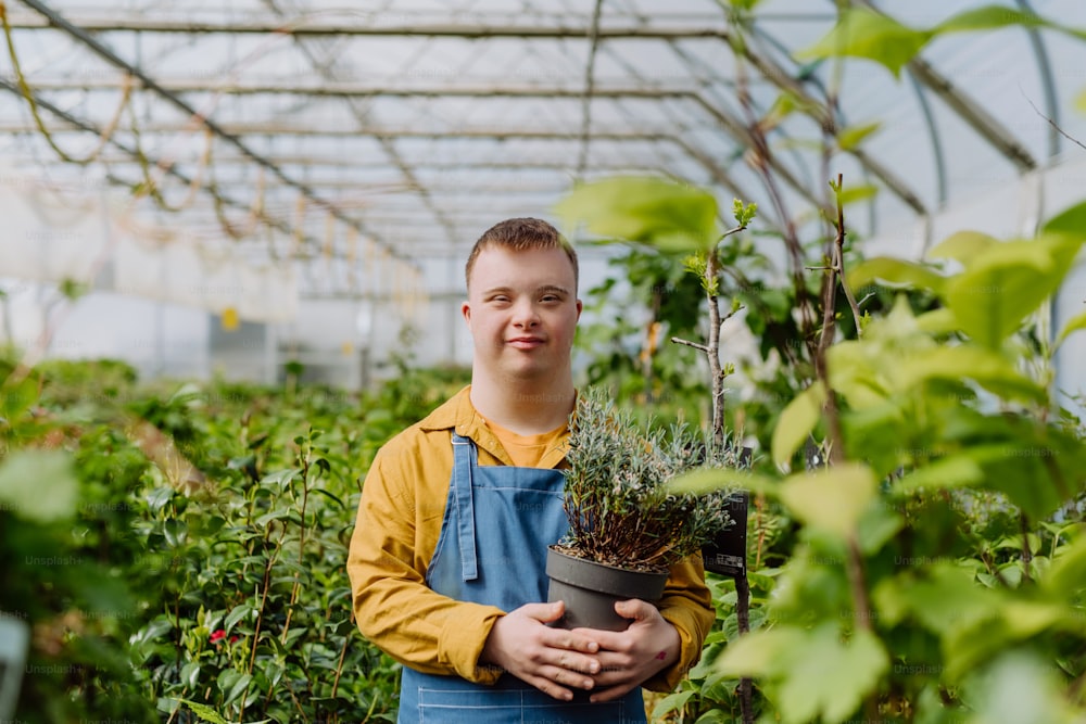 Ein glücklicher junger Mitarbeiter mit Down-Syndrom, der im Gartencenter arbeitet und sich um Blumen kümmert.