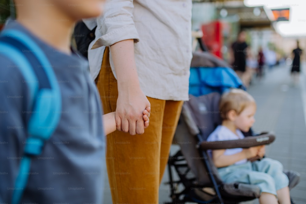 Eine junge Mutter pendelt mit kleinen Kindern auf dem Weg zur Schule, die in der Stadt auf den Bus wartet.