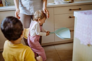 Un niño y una niña ayudan a limpiar la casa con una sartén y un cepillo mientras barren la suciedad del piso.