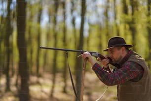 A hunter man aiming with rifle gun on prey in forest.