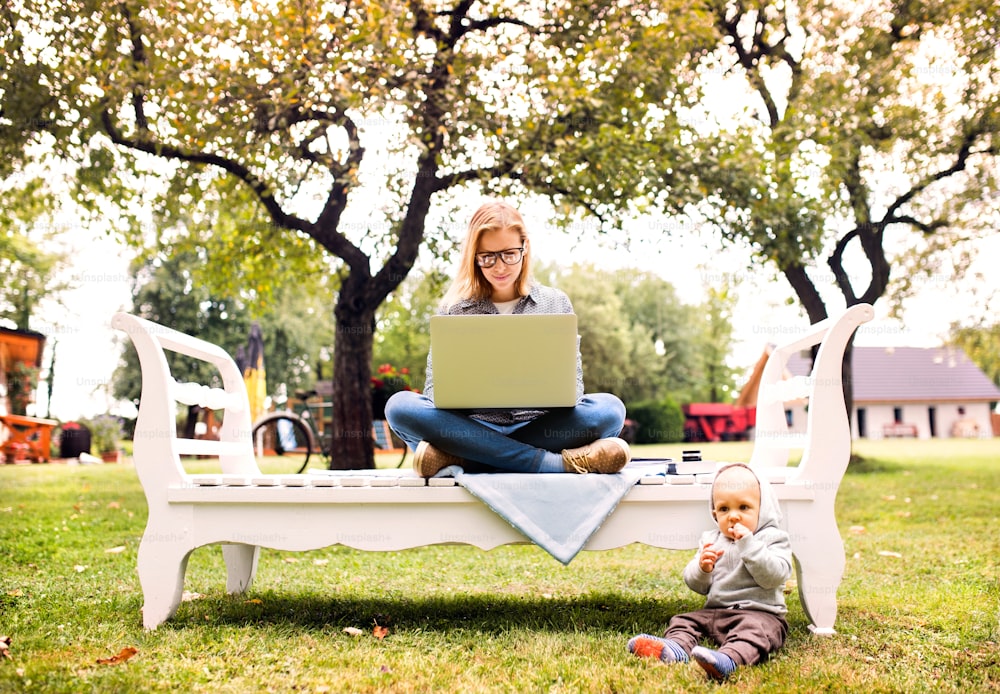 야외에서 공부하는 아기를 안고 있는 아름다운 젊은 여성. 정원에서 노트북을 가진 어머니.