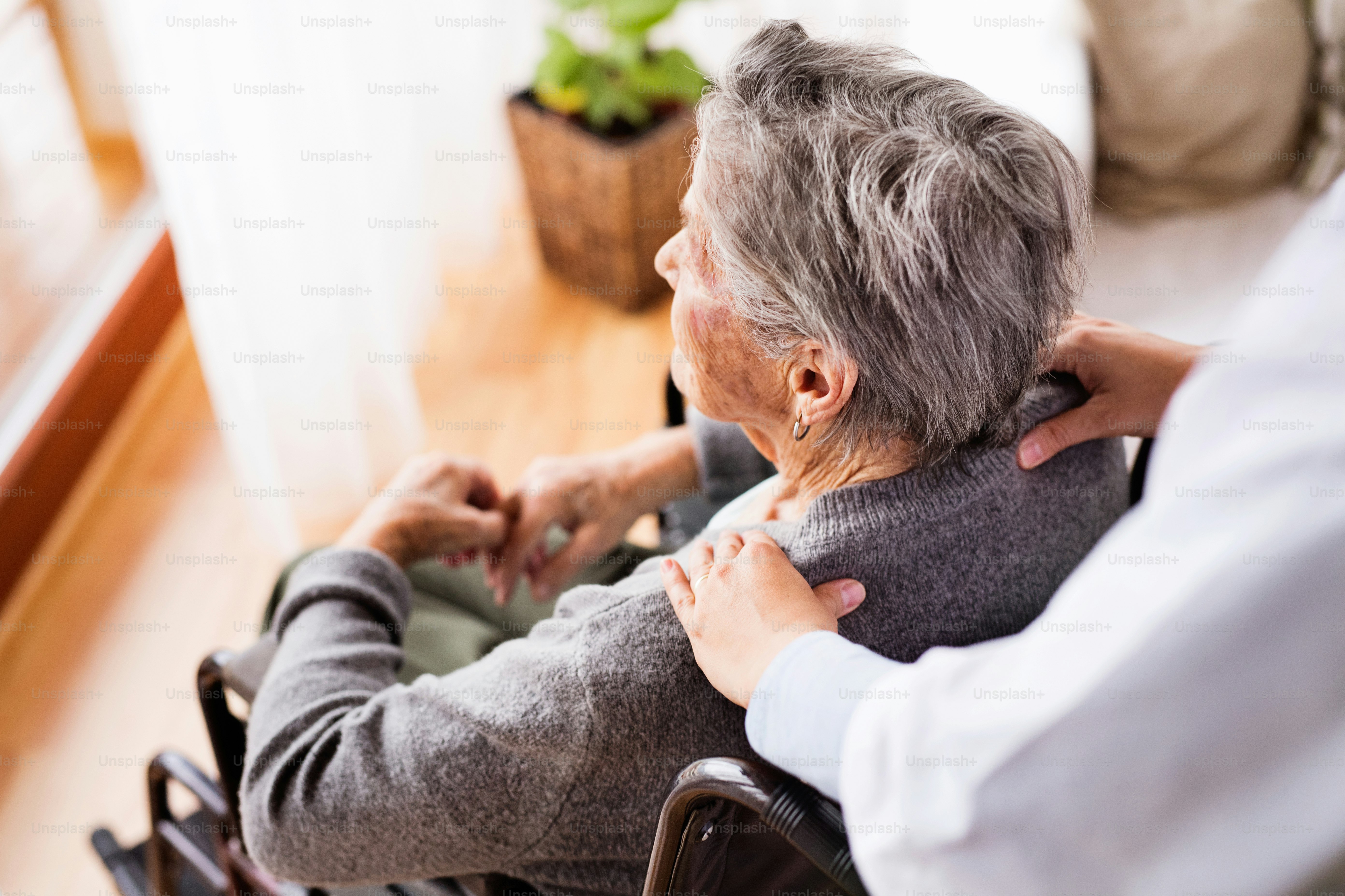 Health visitor and a senior woman during home visit. Unrecognizable nurse giving woman shoulder massage