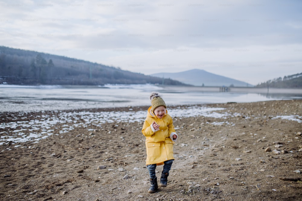 Un niño feliz con Down corriendo afuera junto al lago en invierno.
