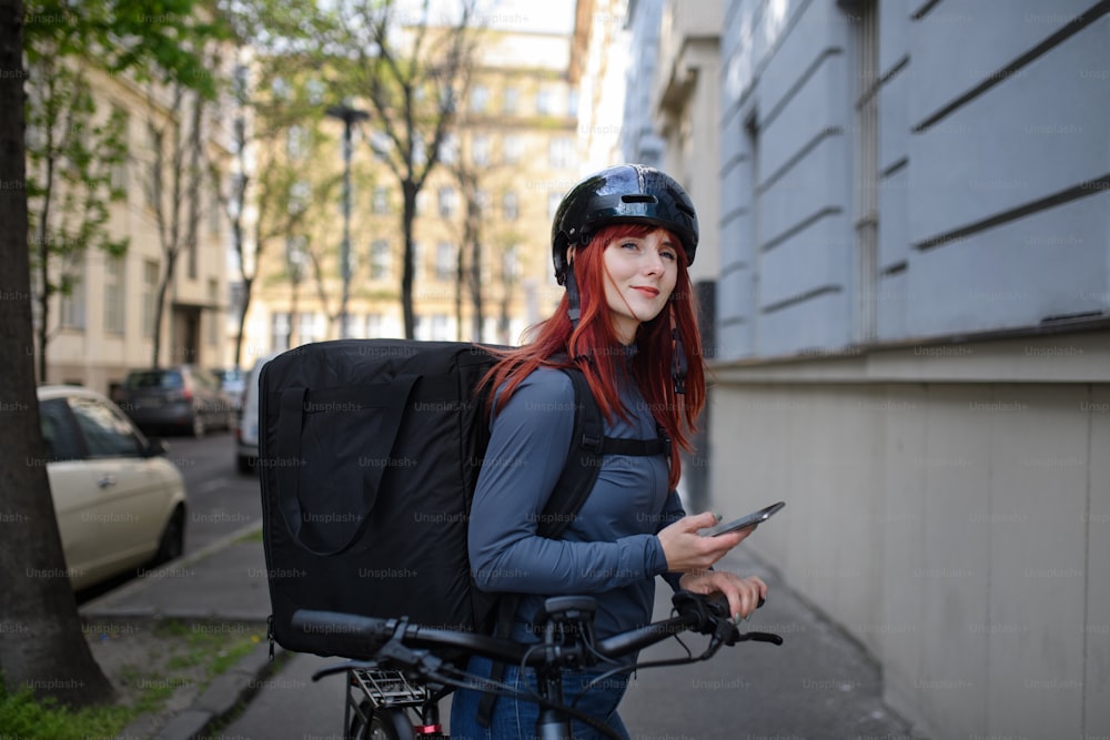 A female courier on bicycle with thermal backpack on way to deliver food to customers.