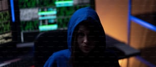 A hooded anonymous hacker by computer in the dark room at night, cyberwar concept.