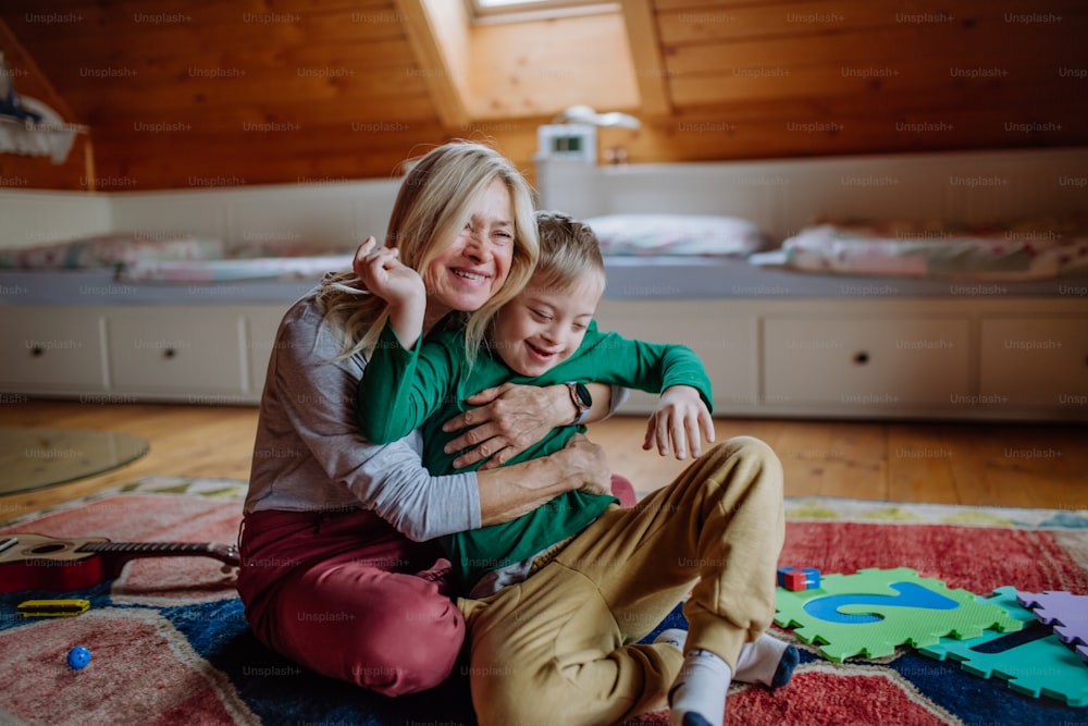 Un ragazzo felice con la sindrome di Down seduto sul pavimento e abbracciato con sua nonna a casa