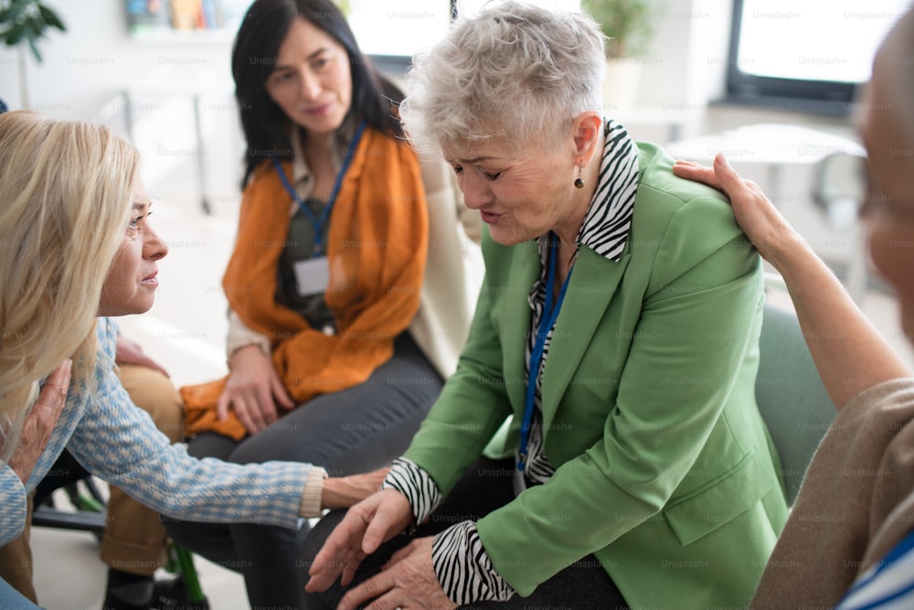 A group of senior people sitting in circle during therapy session, consoling depressed woman.