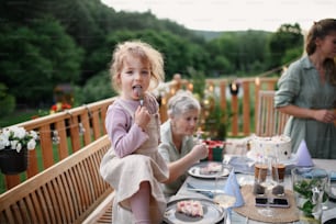 A little girl enjoying eating birthday cake during multi generation family celebration outside on patio.