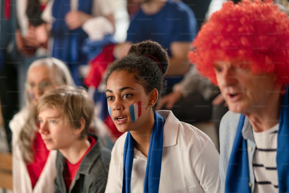 Excited football fans supproting French national team in live soccer match at a stadium.