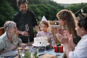 A multi generation family celebratiing birthday of little girl and having garden party outside on patio.