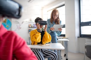 Young high school teacher giving lesson to students with VR goggles in a classroom