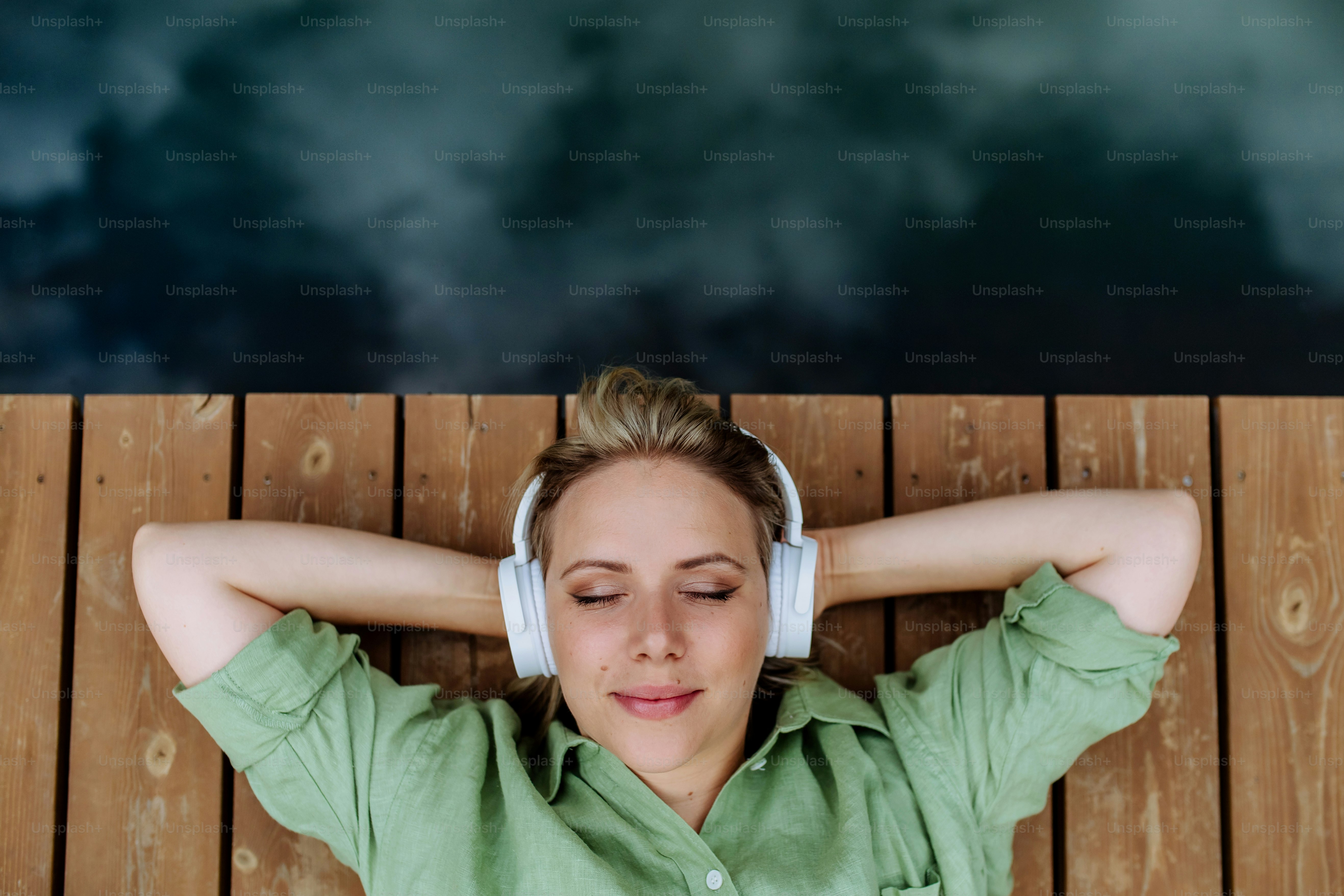 A woman lying down on a wooden floor wearing a high-end pair of over-ear headphones,
practicing intentional music as a therapy and listening to Drake's new album as somatic self-
care.