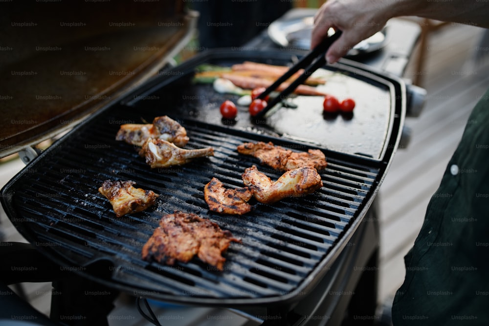 An unrecognizable man grilling meat and vegetable on grill during family summer garden party, close-up