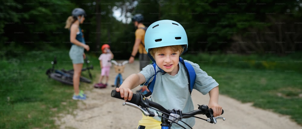 A portrait of excited little boy with his family at backround riding bike on path in park in summer