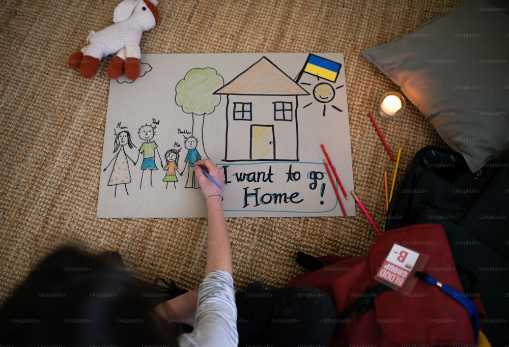 Una vista superior de una colegiala refugiada ucraniana que falta a casa y dibuja a su familia. Concepto de guerra de Ucrania.