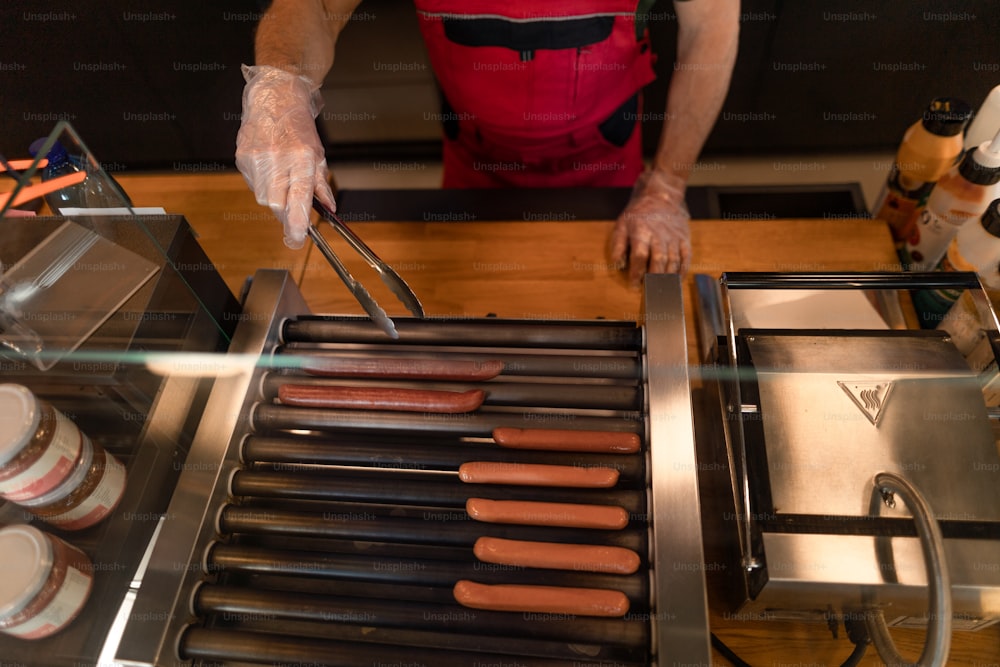 Un primer plano de un camarero parado junto al mostrador y preparando perritos calientes a un cliente en la cafetería de la gasolinera.