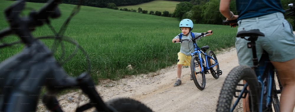 Un ritratto di ragazzino eccitato con la sua famiglia a cavallo in bicicletta sul sentiero nel parco in estate