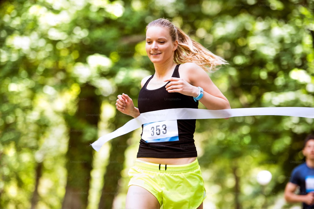 Belle jeune femme courant la course en franchissant la ligne d’arrivée.