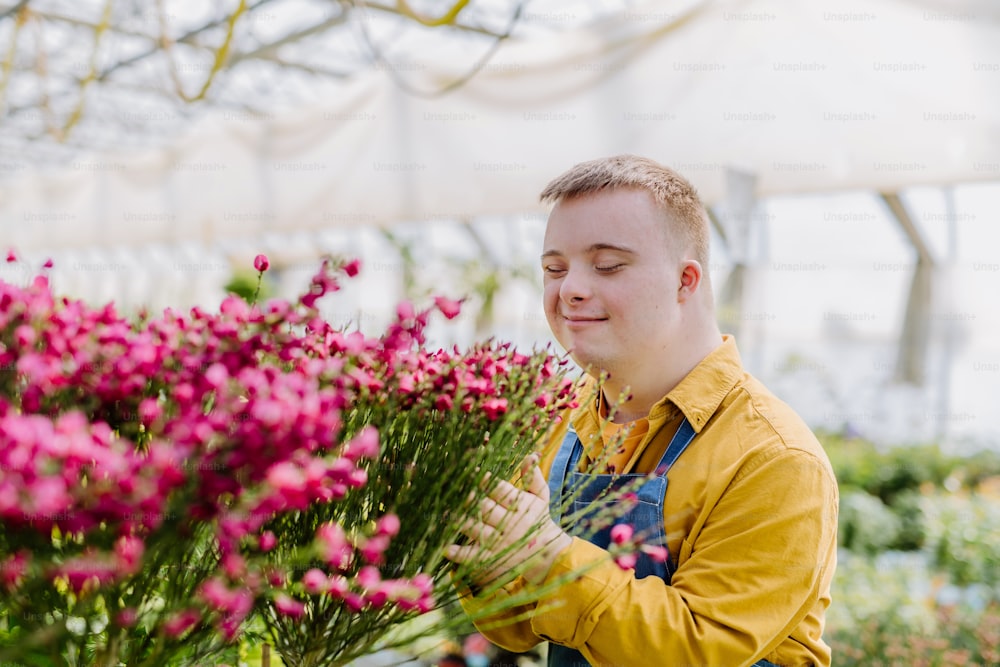 다운 증후군을 앓고있는 행복한 젊은 직원이 정원 센터에서 꽃을 돌보고 있습니다.