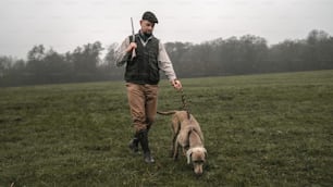A hunter man with dog in traditional shooting clothes on field holding shotgun.