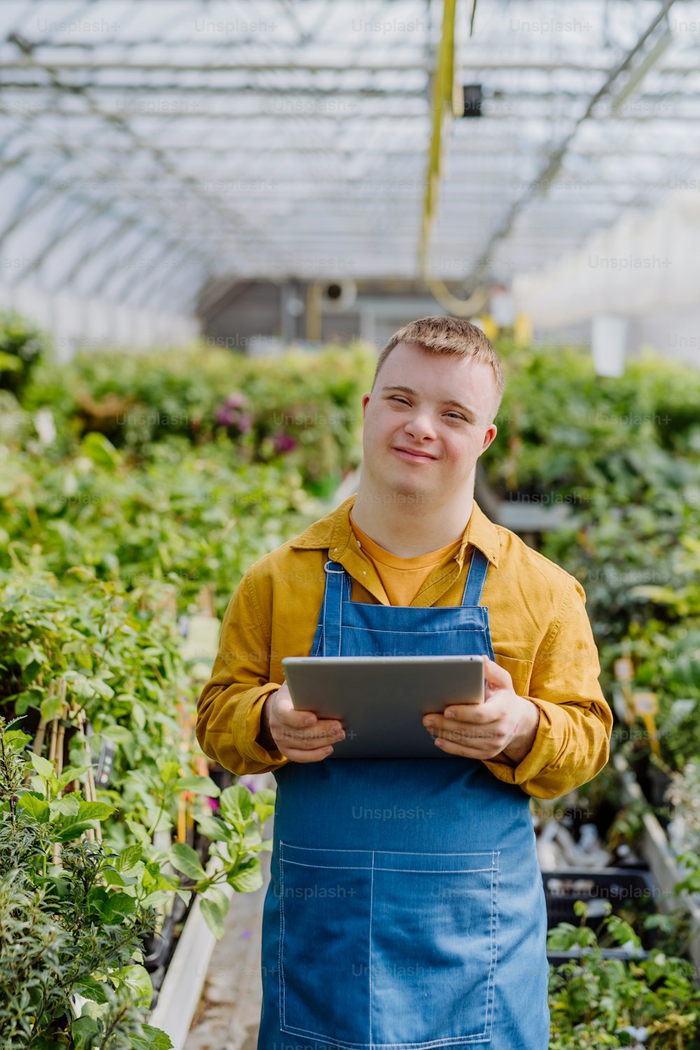 Un jeune homme atteint du syndrome de Down travaille dans une jardinerie, dans un presse-papiers et vérifie des plantes.