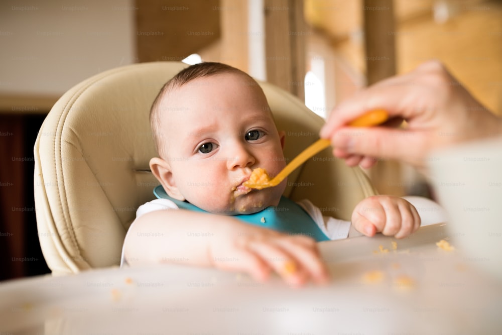スプーンを使って赤ん坊の息子に餌をやる見分けがつかない母親。