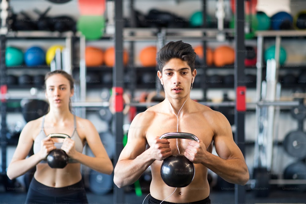 Lindo casal jovem em forma fazendo treinamento de força, exercitando-se com kettlebell na academia moderna.