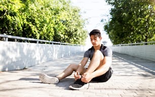 靴紐を結んでコンクリートの道に座っている街の若いヒスパニック系ランナー。