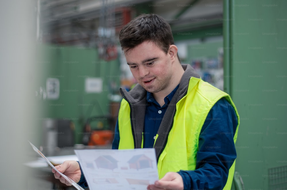 A young man with Down syndrome looking at blueprints when working in industrial factory, social integration concept.