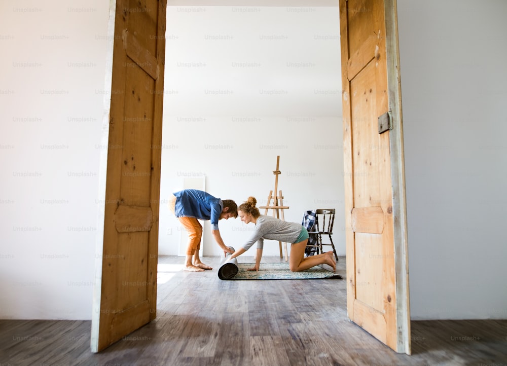 Young married couple moving in new house, rolling out carpet.