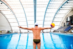 Water polo player in a swimming pool. Man doing sport. Rear view.