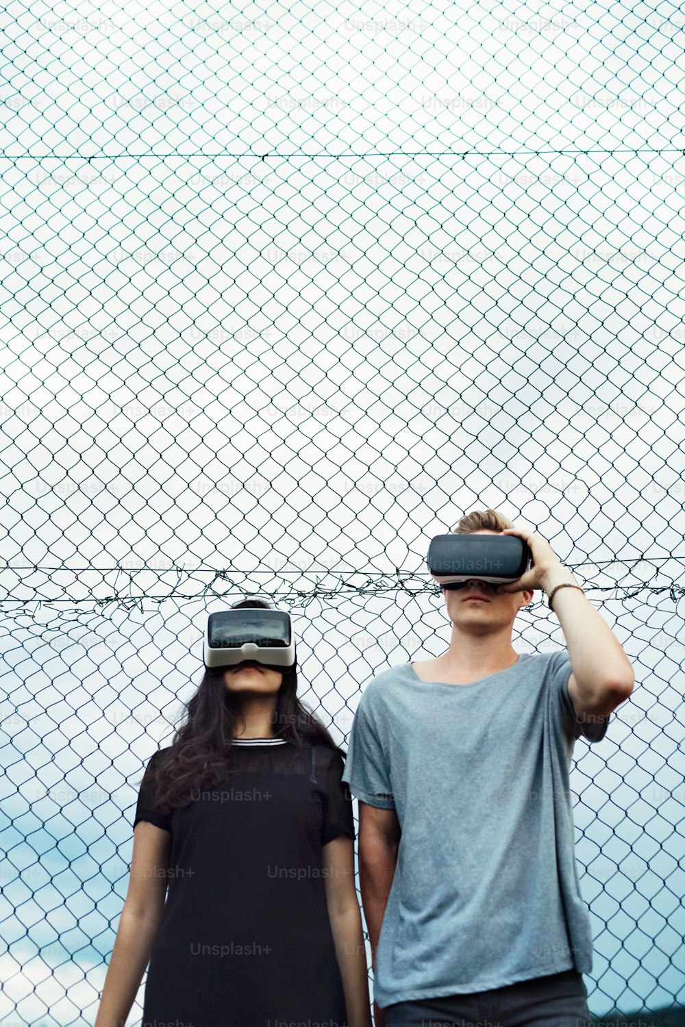 Attractive teenage couple outdoors on playground wearing virtual reality goggles.
