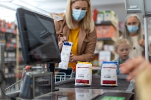 A young woman shopping in supermarket, putting products on checking desk during pandemic