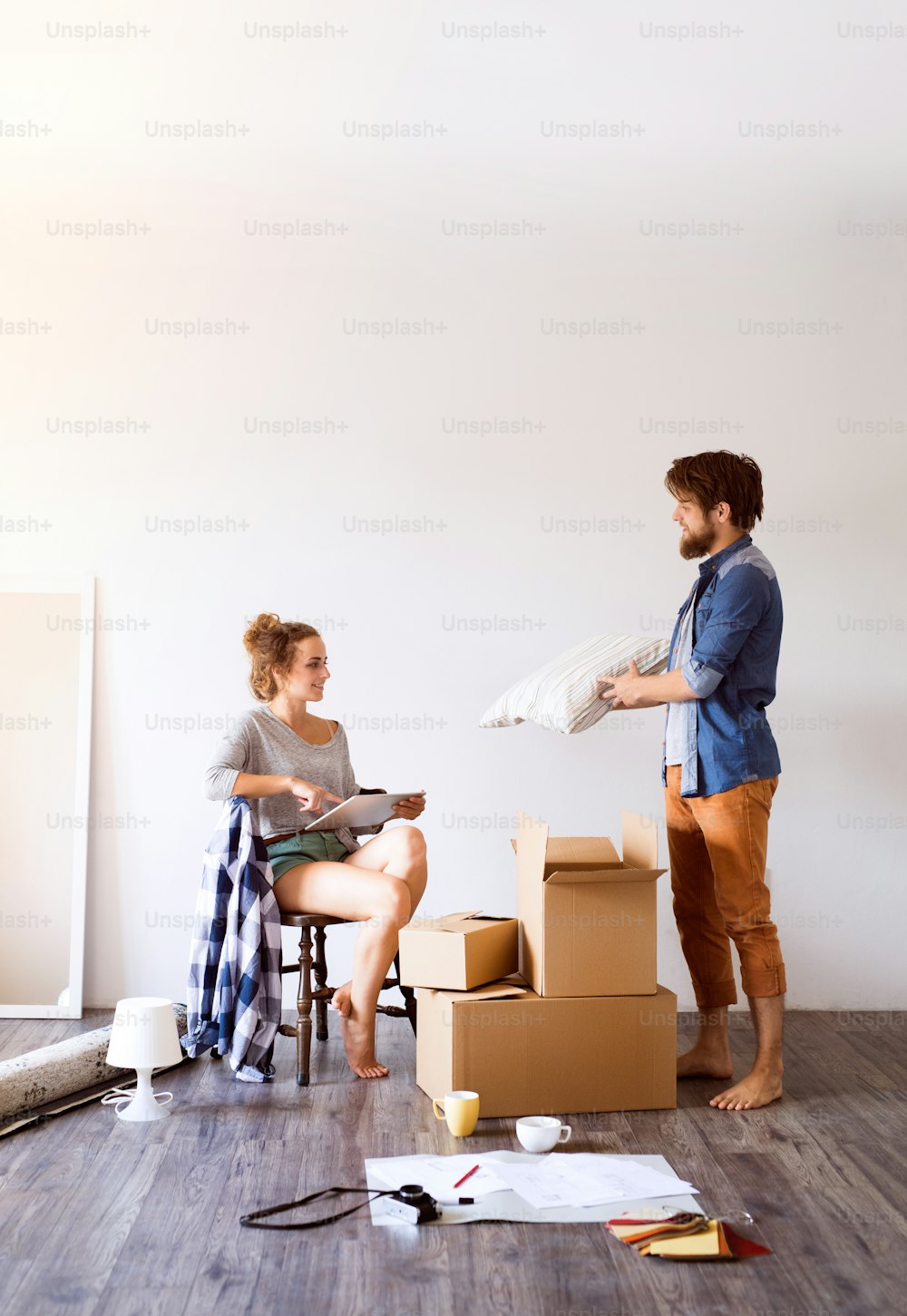 Young married couple moving in new house, sitting on the floor near cardboard boxes, drinking coffee.
