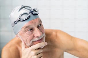 Senior man standing in an indoor swimming pool. Active pensioner enjoying sport.