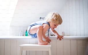 Little toddler boy climbing out of bathtub. Domestic accident. Dangerous situation in the bathroom.