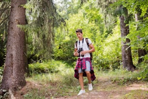 Teenage boy with binoculars hiking in forest. Summer vacation adventure.