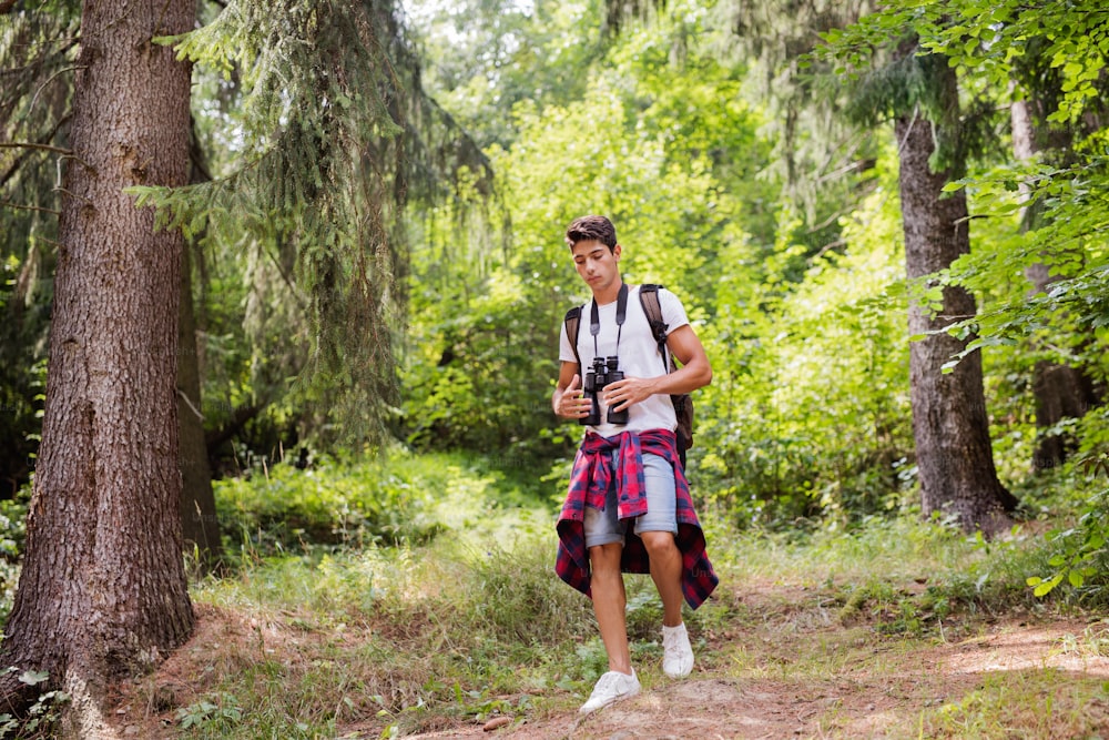 Teenage boy with binoculars hiking in forest. Summer vacation adventure.
