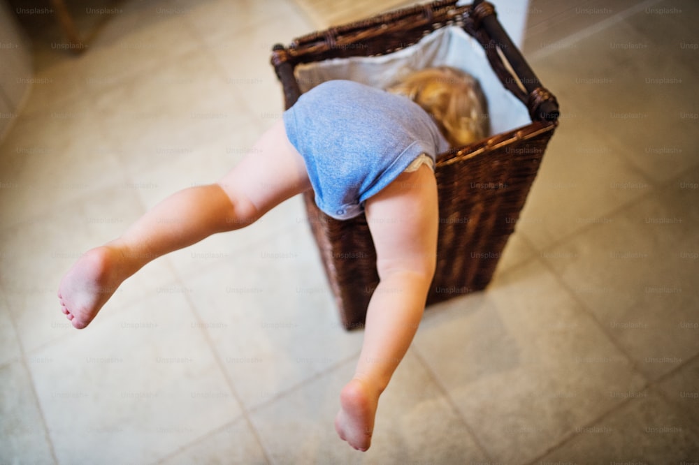 Niño pequeño en una situación peligrosa en el baño. Un niño pequeño en un cesto de ropa sucia, con las piernas sobresaliendo.