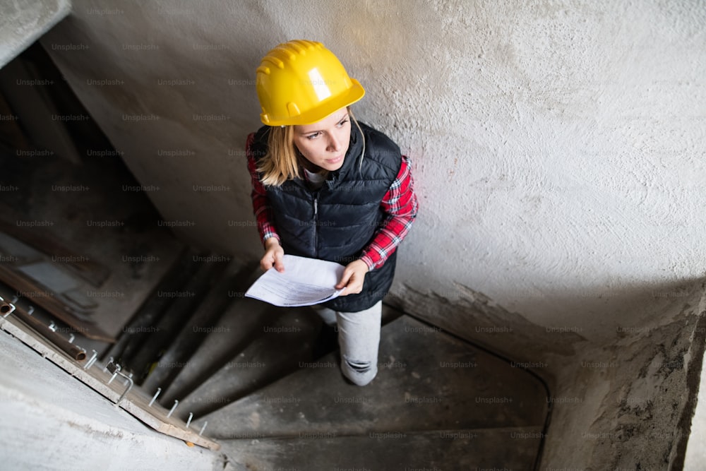 Female worker on the building site. Beautiful young woman holding blueprints. House construction. Top view.