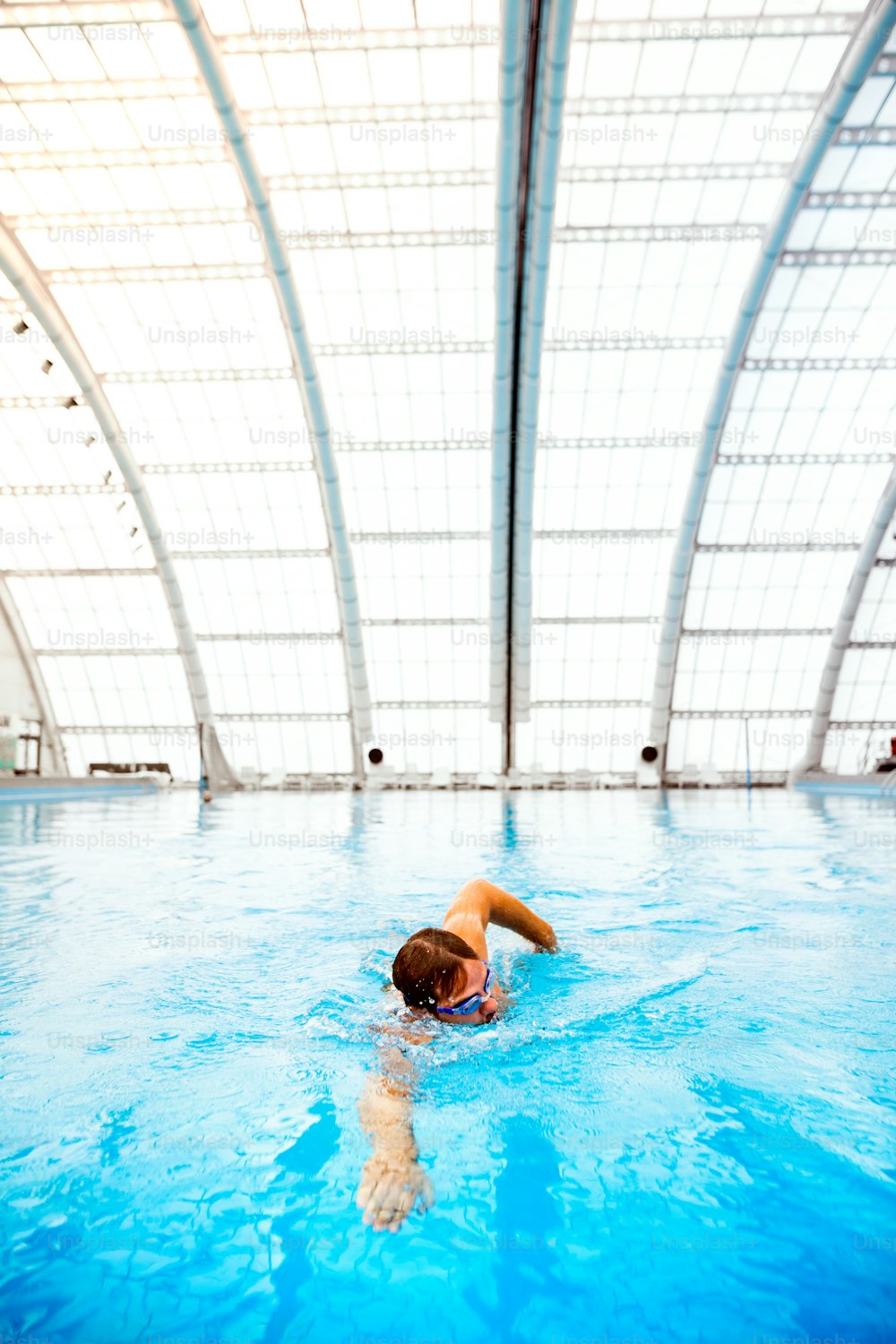 Uomo che nuota in una piscina coperta. Nuotatore professionista che si allena in piscina.