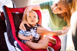Giovane madre che mette il suo bambino nel seggiolino auto, allacciando le cinture di sicurezza.